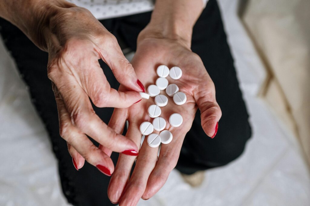 pexels photo 4661296 4661296 Senior woman's hands with red nails holding circular white tablets, depicting medication concept.